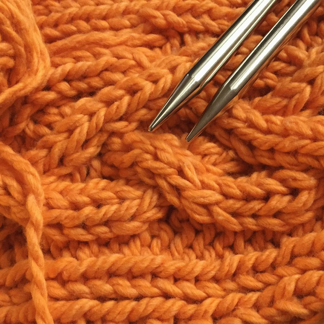 A knitting project with bulky orange cables.