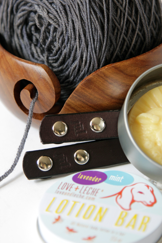 A closer look at the Read Along Crochet Along prize pack on Hands Occupied, featuring a Darn Good Yarn yarn bowl, bag handles from Jul Designs, a Love & Leche lotion bar, and yarn from Why Knot Fibers.