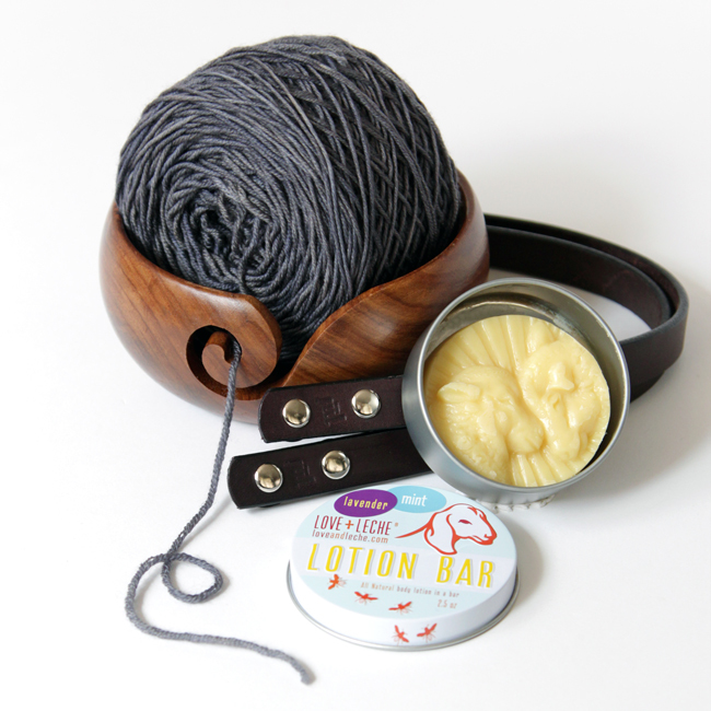 A closer look at the Read Along Crochet Along prize pack on Hands Occupied, featuring a Darn Good Yarn yarn bowl, bag handles from Jul Designs, a Love & Leche lotion bar, and yarn from Why Knot Fibers.