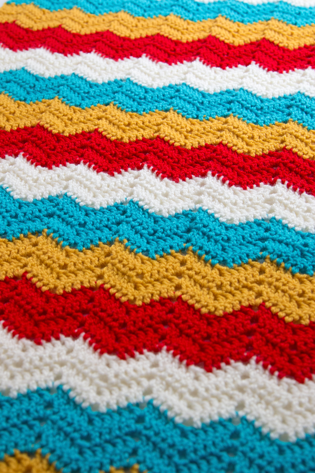 Get your hands on the free crochet pattern for the Ripple Wrap! The Ripple Wrap is a four-color take on one of the most universally-recognized crochet stitches: the ripple stitch. Seen in afghan patterns in grandmothers' houses everywhere, the ripple stitch creates a fun zig zag pattern that opens up tons of possibilities for color combos.