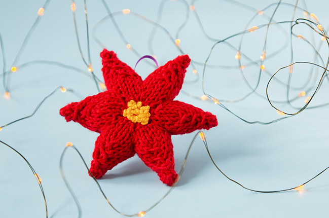 Trim your tree with a hand knit ornament! This festive poinsettia will add a splash of color to your holiday decor. Click through for the free knitting pattern.