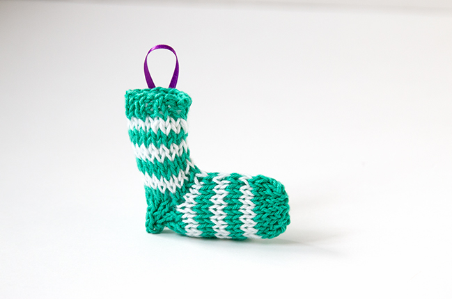 A tiny knit stocking is the most adorable way to trim your tree! Get the free knitting pattern for this striped stocking. #christmasornament #stockingornament #freeknittingpattern