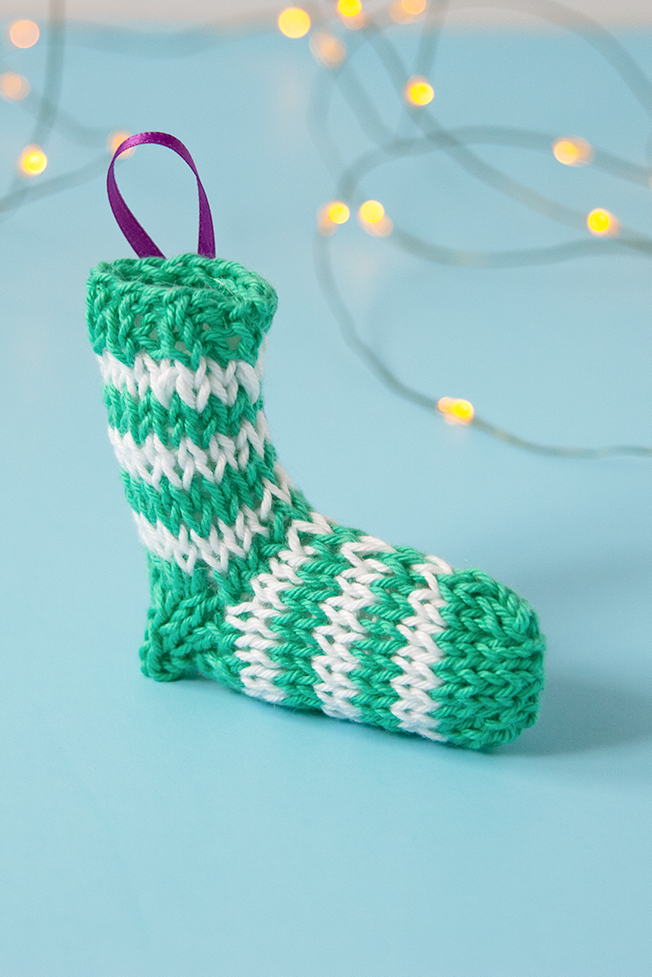 A tiny knit stocking is the most adorable way to trim your tree! Get the free knitting pattern for this striped stocking. #christmasornament #stockingornament #freeknittingpattern