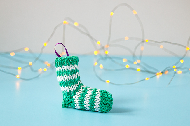 A tiny knit stocking is the most adorable way to trim your tree! Get the free knitting pattern for this striped stocking. #christmasornament #stockingornament #freeknittingpattern