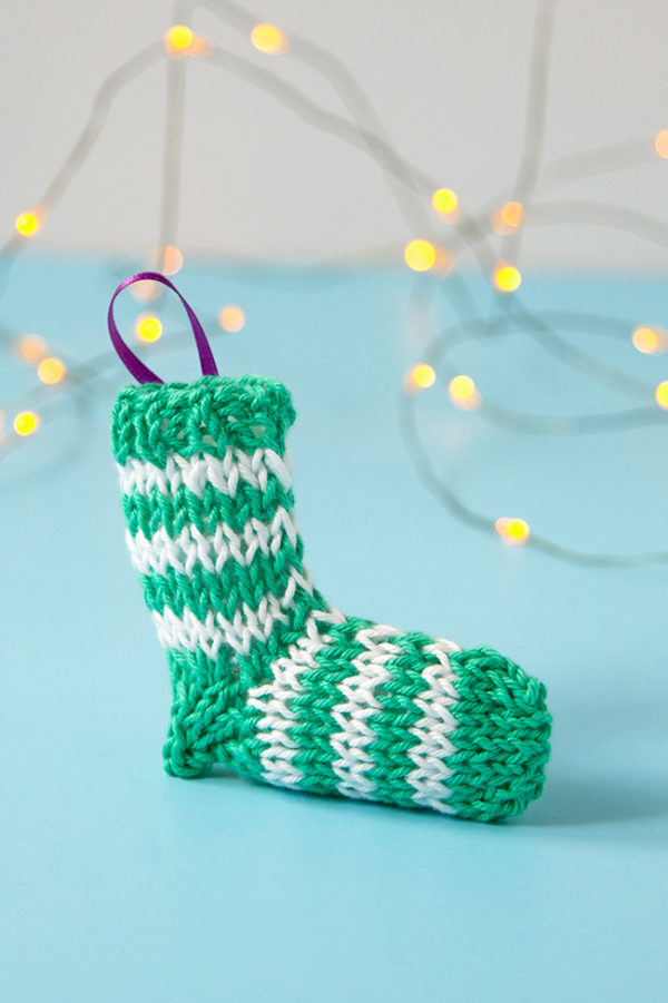 A tiny knit stocking is the most adorable way to trim your tree! Get the free knitting pattern for this striped stocking. #christmasornament #stockingornament #freeknittingpattern