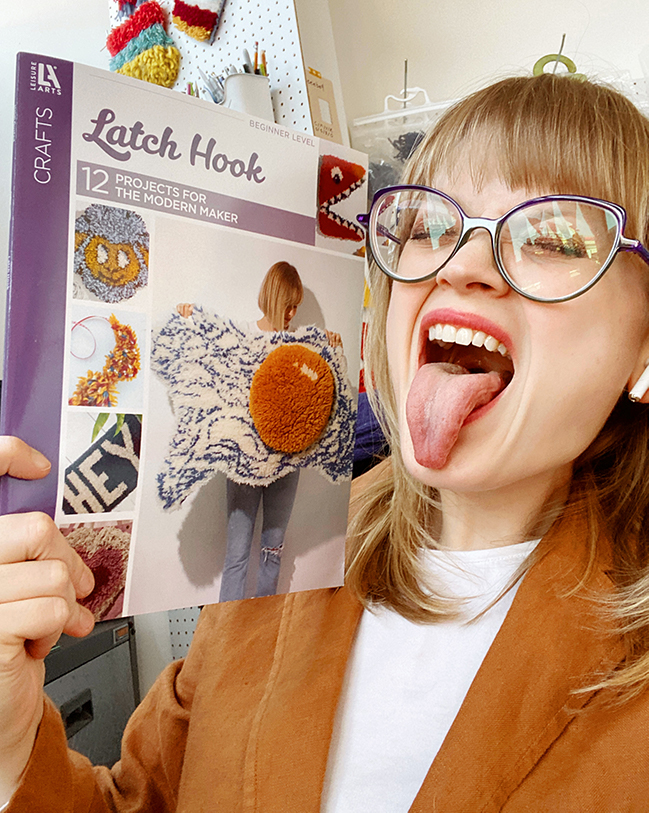 Heidi Gustad reacts to holding a copy of her first book Latch Hook: 12 Projects for the Modern Maker. She's sitting in her Chicago craft studio.