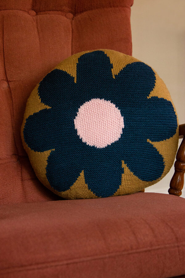 A round Intarsia Flower Pillow sits on a rocking chair.