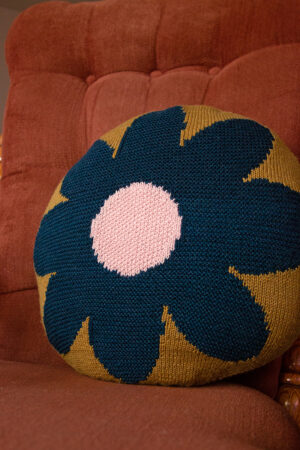 A round Intarsia Flower Pillow sits on a rocking chair.